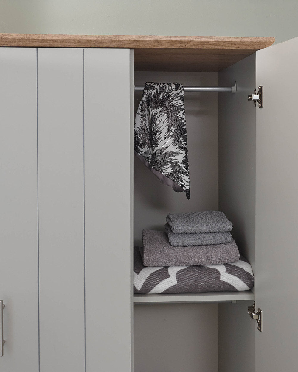 A 3 door wardrobe in modern subtle grey offers ample storage space and elegant brushed steel handles. The wardrobe opens to reveal hanging space and a convenient shelf. It also features three drawers with cup handles. The muted grey colour complements any interior style and contrasts with the oak-effect top. The wardrobe is aesthetically pleasing and sturdy, with a deep base plinth. It comes flat packed for self-assembly. Delivery is available only to mainland UK, excluding certain postcodes.