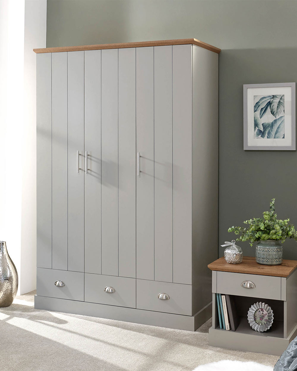 A 3 door wardrobe in modern subtle grey offers ample storage space and elegant brushed steel handles. The wardrobe opens to reveal hanging space and a convenient shelf. It also features three drawers with cup handles. The muted grey colour complements any interior style and contrasts with the oak-effect top. The wardrobe is aesthetically pleasing and sturdy, with a deep base plinth. It comes flat packed for self-assembly. Delivery is available only to mainland UK, excluding certain postcodes.