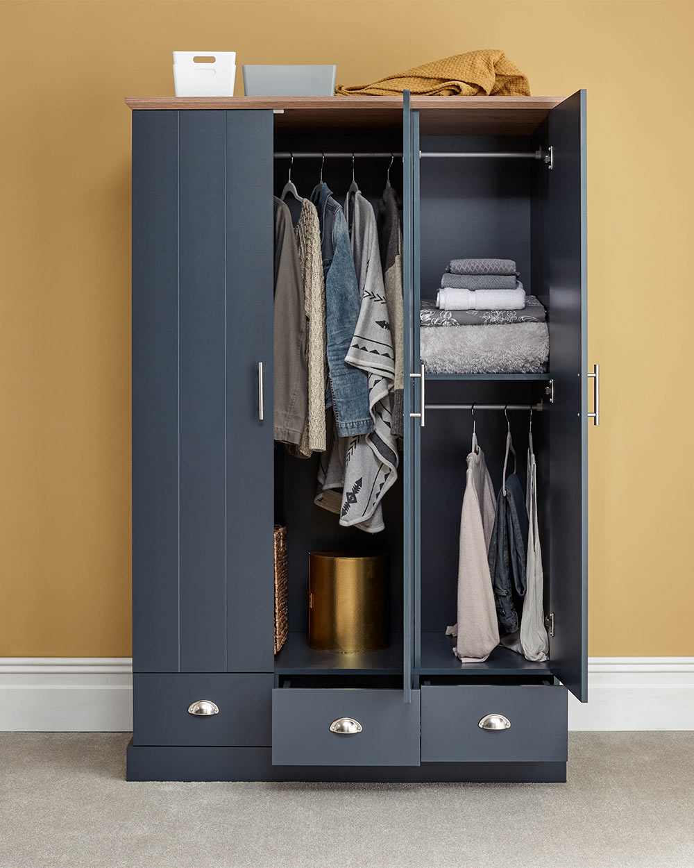 A 3 door wardrobe in modern slate blue offers ample storage space and elegant brushed steel handles. The wardrobe opens to reveal hanging space and a convenient shelf. It also features three drawers with cup handles. The bold slate blue colour complements any interior style and contrasts with the oak-effect top. The wardrobe is aesthetically pleasing and sturdy, with a deep base plinth. It comes flat packed for self-assembly. Delivery is available only to mainland UK, excluding certain postcodes.