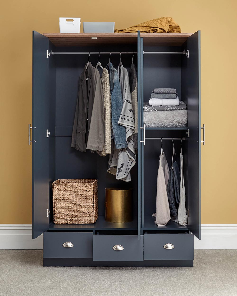A 3 door wardrobe in modern slate blue offers ample storage space and elegant brushed steel handles. The wardrobe opens to reveal hanging space and a convenient shelf. It also features three drawers with cup handles. The bold slate blue colour complements any interior style and contrasts with the oak-effect top. The wardrobe is aesthetically pleasing and sturdy, with a deep base plinth. It comes flat packed for self-assembly. Delivery is available only to mainland UK, excluding certain postcodes.