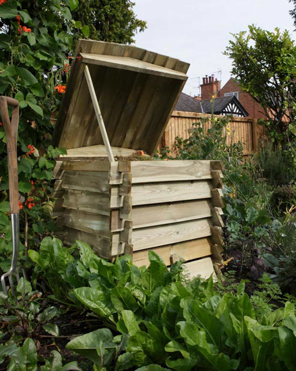 Garden compost bin in the shape of a beehive pictured in someone's garden. Rowlinson beehive composter with the lid up on the hinges