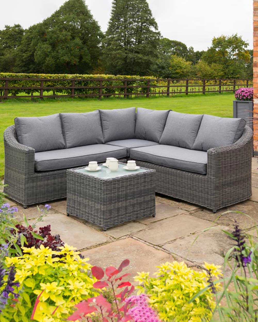 rattan corner sofa set garden furniture in modern grey with thick padded cushions and coffee table photographed in a beautiful garden