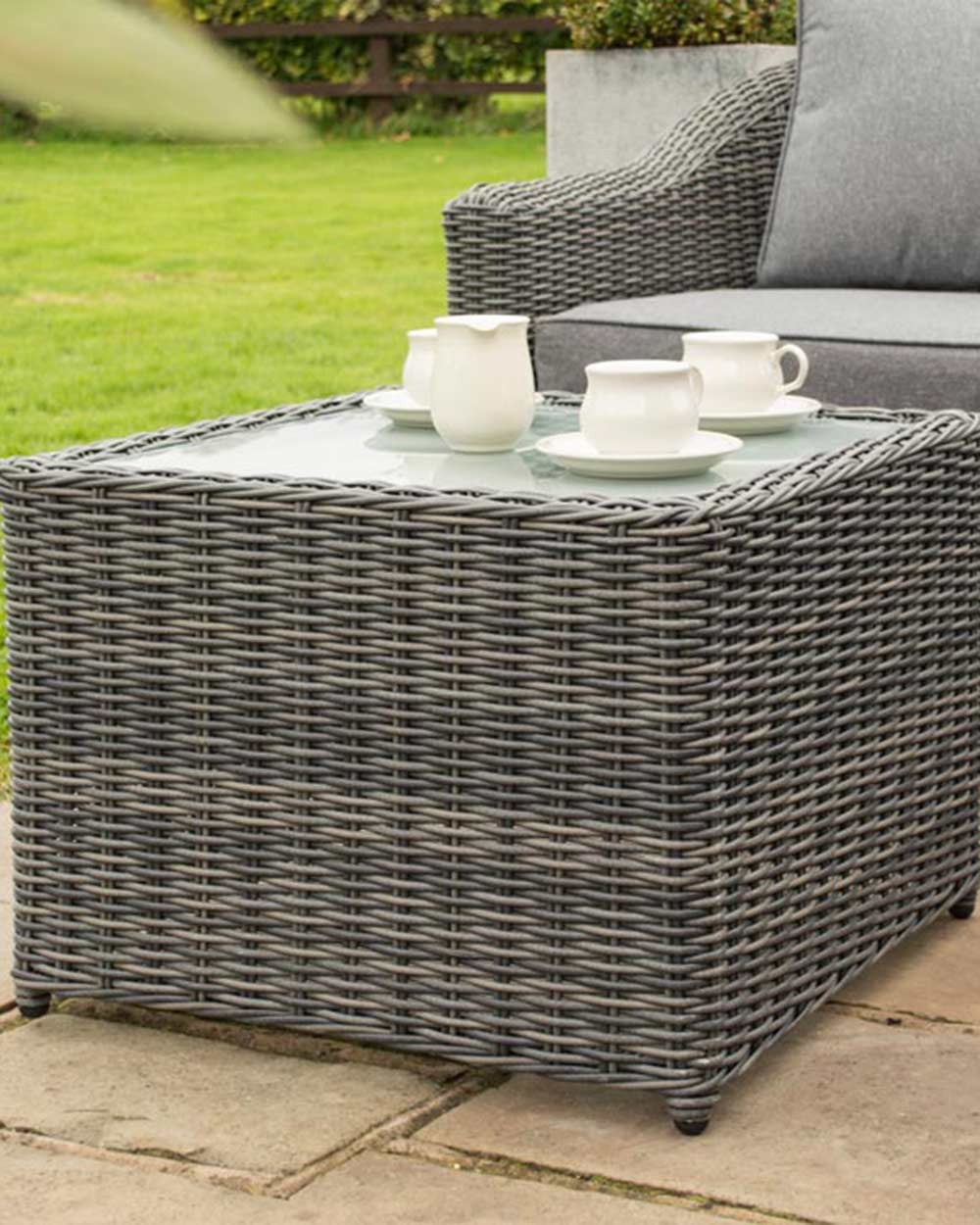 rattan corner sofa set garden furniture in modern grey with thick padded cushions and coffee table photographed in a beautiful garden. Close up of the coffee table