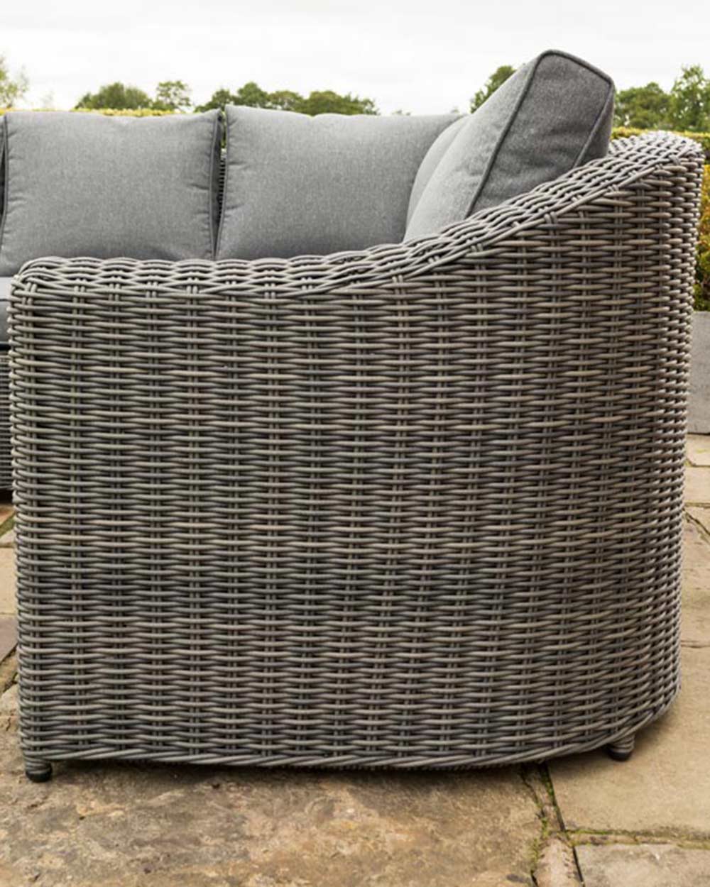 rattan corner sofa set garden furniture in modern grey with thick padded cushions and coffee table photographed in a beautiful garden. Close up of the sofa arms