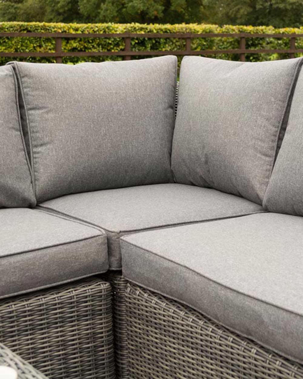 rattan corner sofa set garden furniture in modern grey with thick padded cushions and coffee table photographed in a beautiful garden. Close up of the thick padded cushions