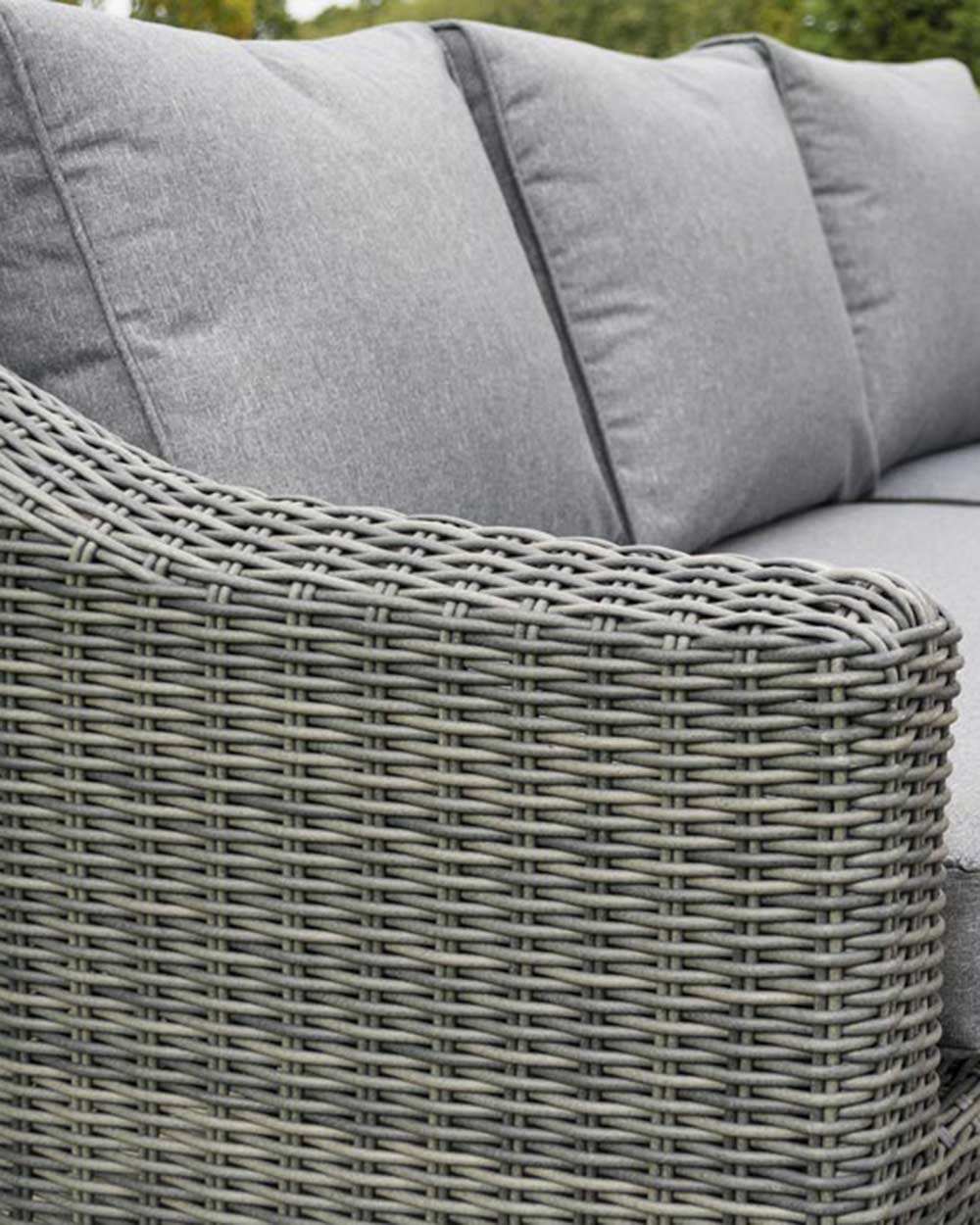 rattan corner sofa set garden furniture in modern grey with thick padded cushions and coffee table photographed in a beautiful garden. Close up of the sofa