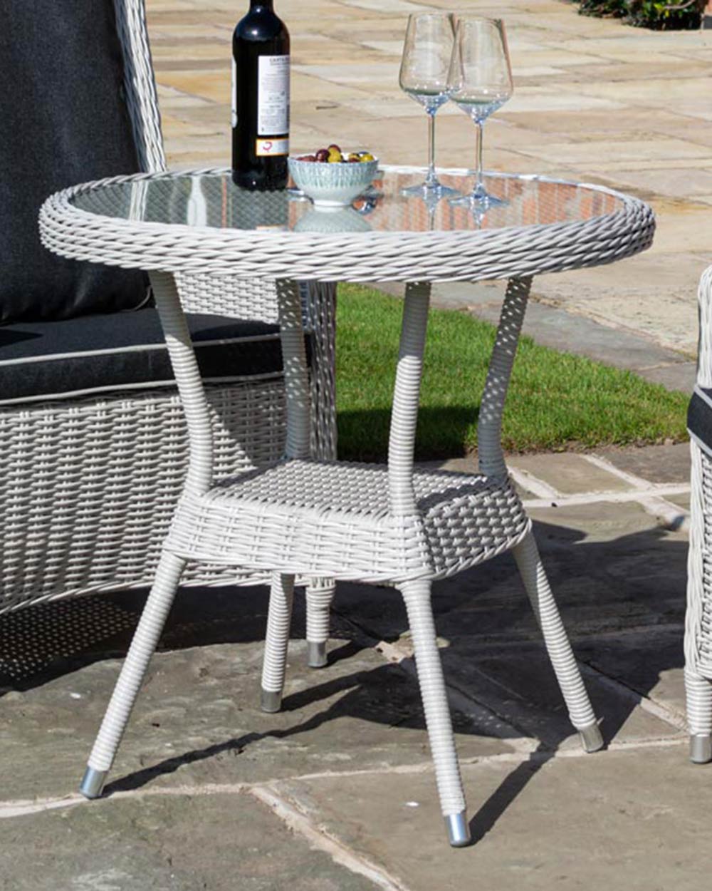 rattan bistro set weather proof in a garden setting with snacks and wine on the glass top table close up