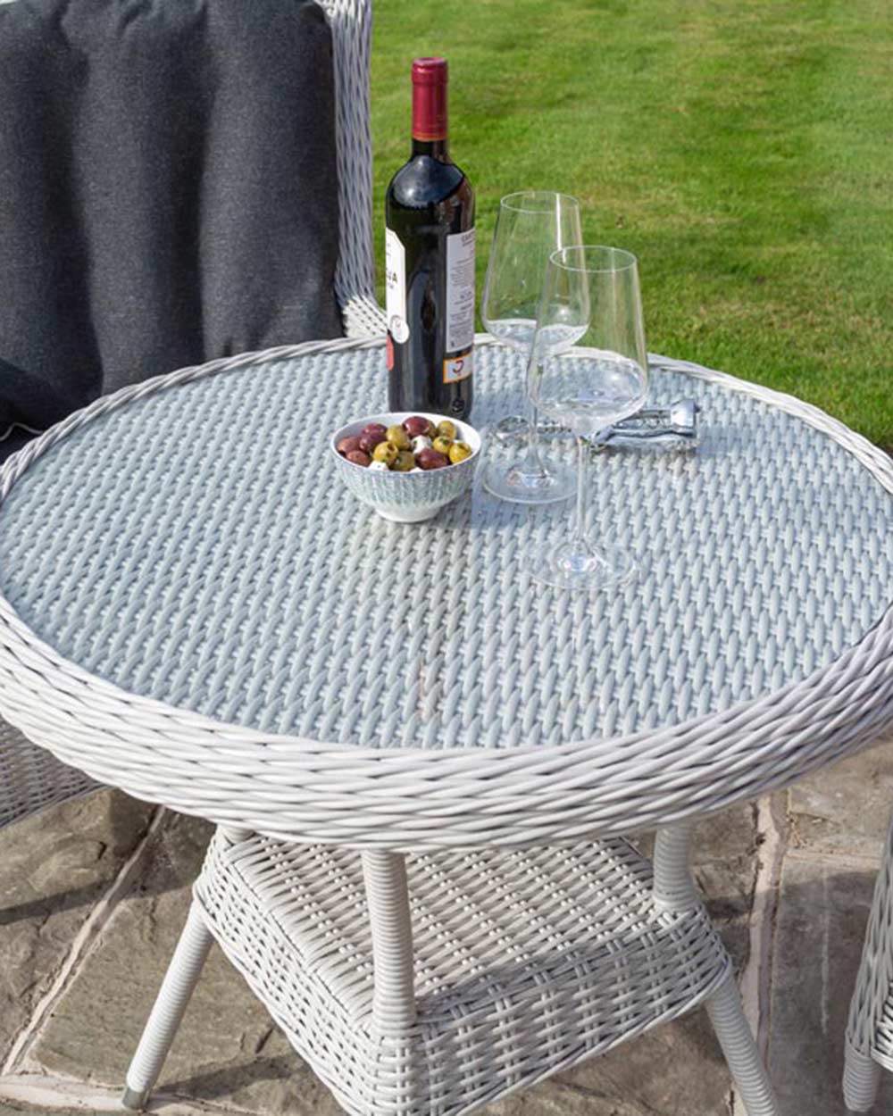 rattan bistro set weather proof in a garden setting with snacks and wine on the glass top table close up