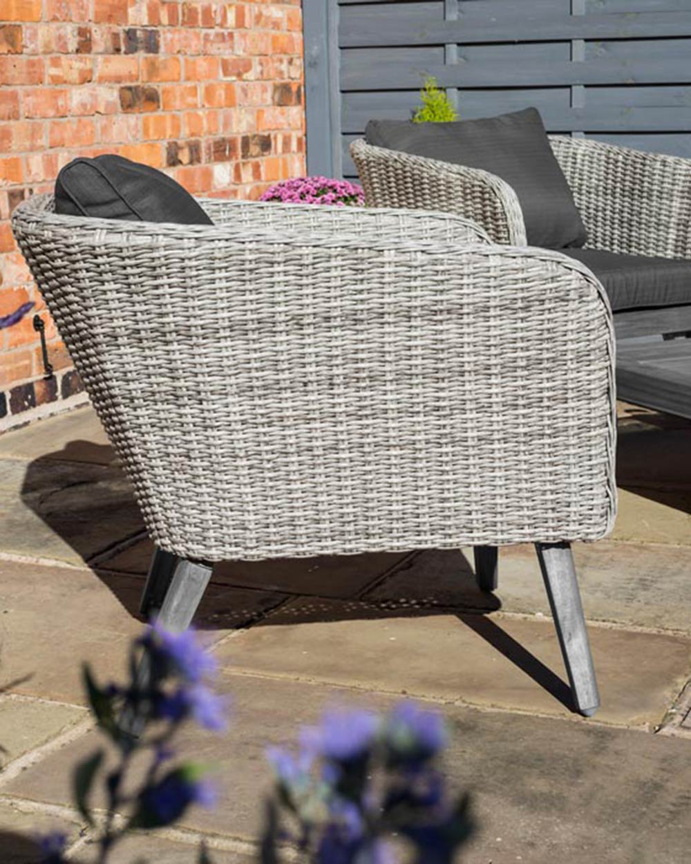 rattan garden furniture sofa set displayed in a garden with a jug of juice and glasses on the hardwood table. Close up of the armchair