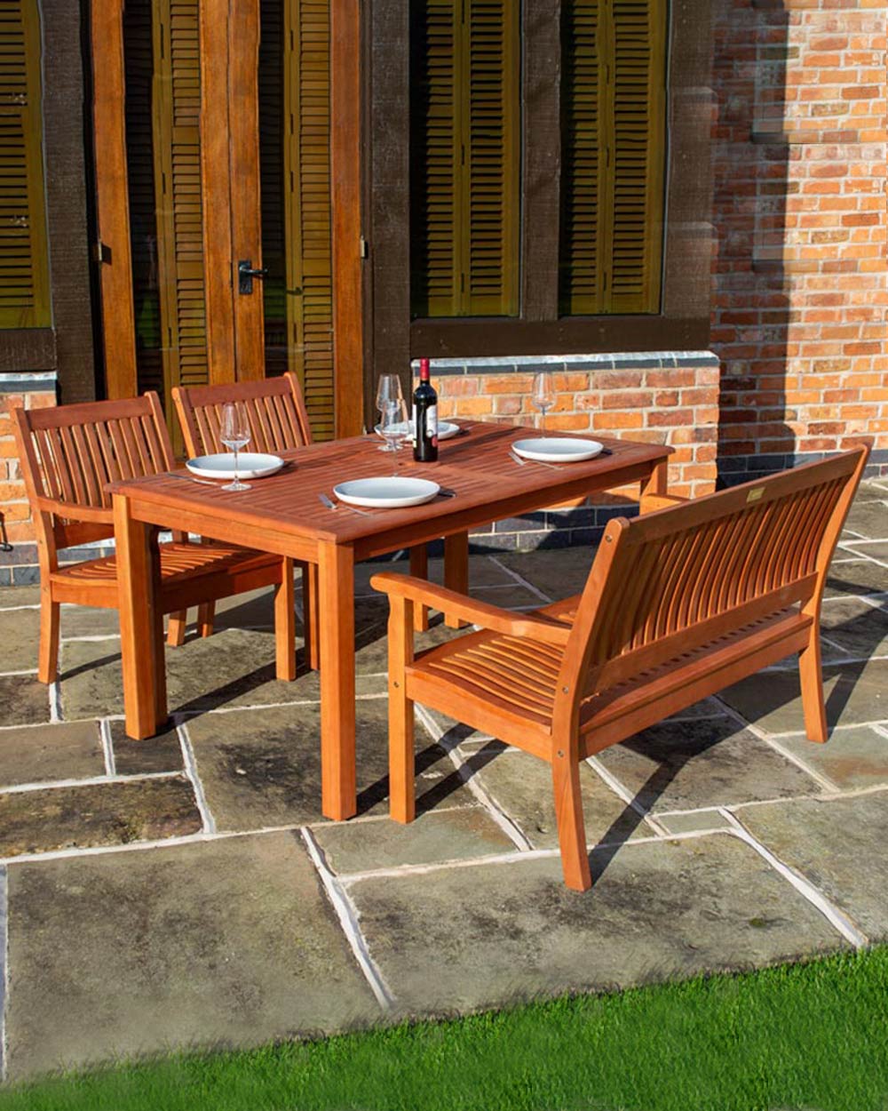 wooden garden furniture set with a rectangular table, 2 arm chairs and a wooden bench photographed on a patio.