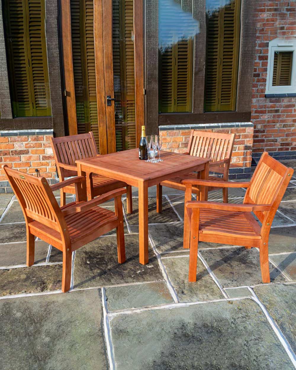wooden garden table and chairs set in a lifestyle setting on a patio. With a bottle of prosecco on the table with some glasses