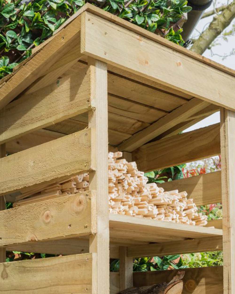 Slim log store narrow outdoor storage for wood kindling. Photographed in the garden with wood and kindling stored inside. Close up of the top of the kindling shelf