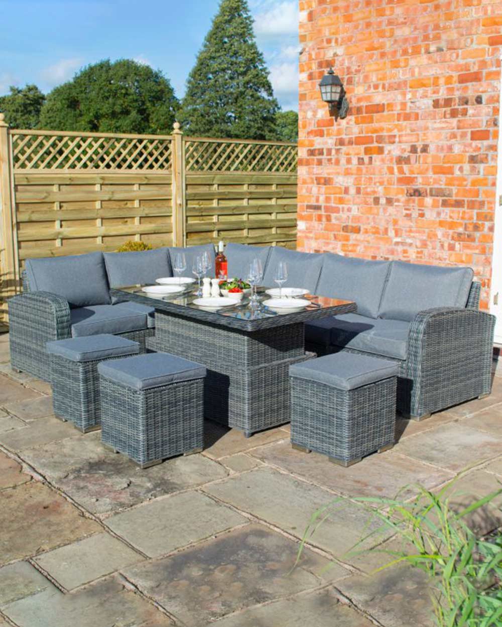 corner dining rattan furniture set with rising table in grey. Lifestyle image of the set on a patio with a the table set for an evening meal