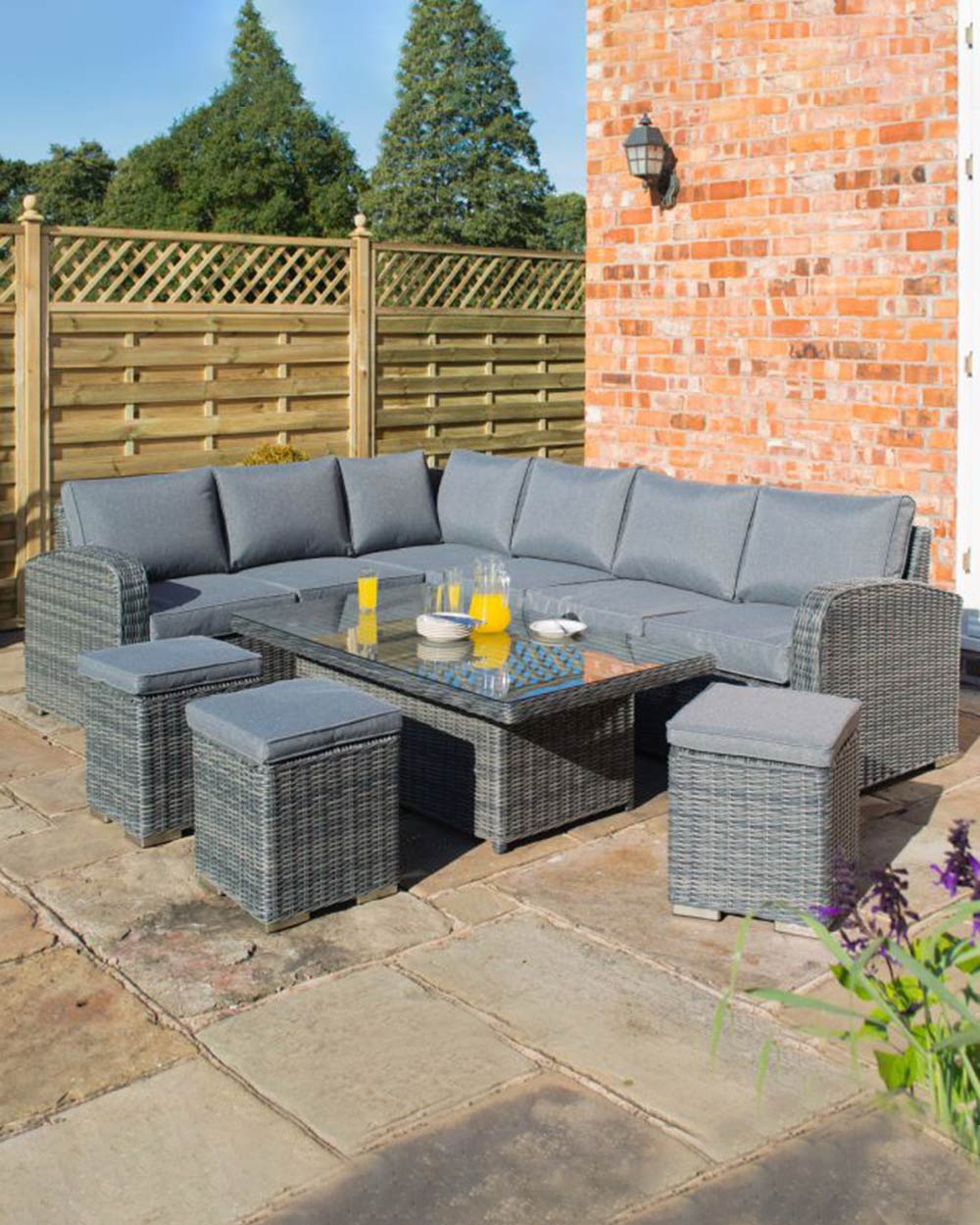 corner dining rattan furniture set with rising table in grey. Lifestyle image of the set on a patio with a jug of juice and glasses on the table