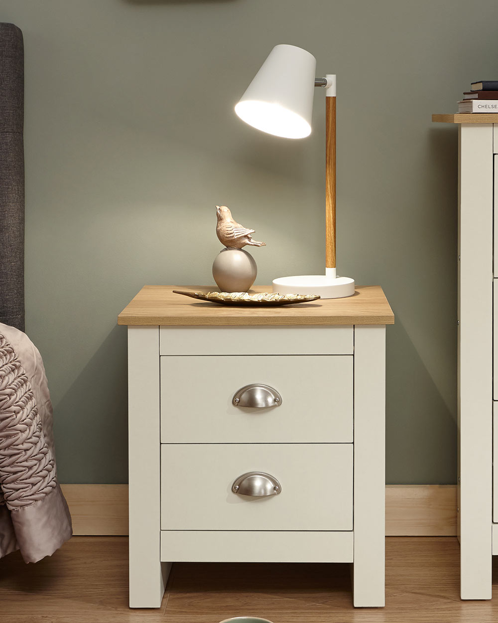 Lancaster bedside cabinet in cream with an oak effect top in a bedroom lifestyle setting with a lamp and decorative accessories on top