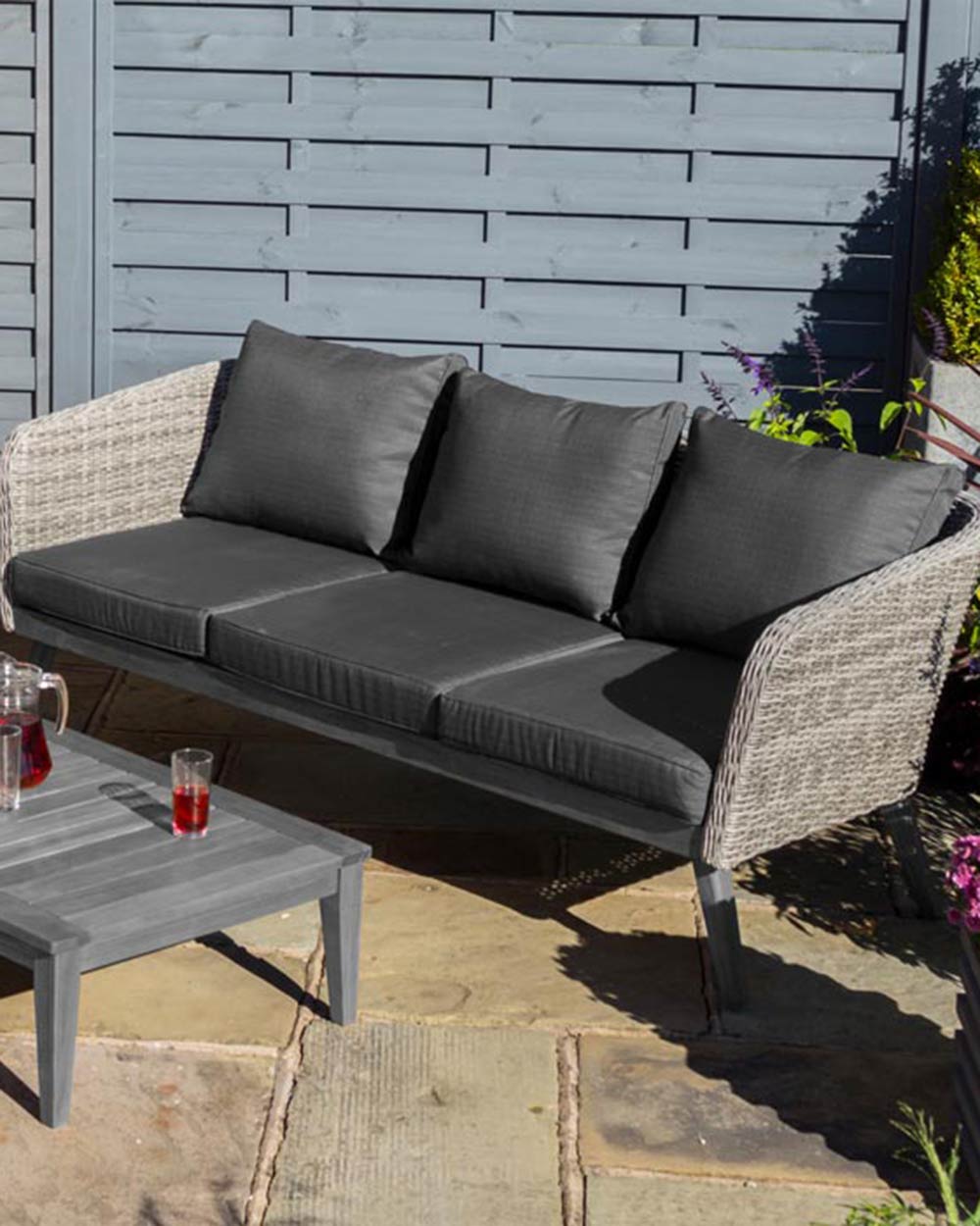 rattan garden furniture sofa set displayed in a garden with a jug of juice and glasses on the hardwood table. close up of the 3 seater sofa