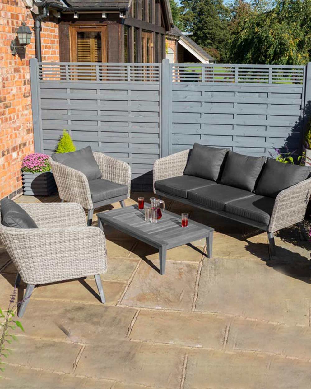 rattan garden furniture sofa set displayed in a garden with a jug of juice and glasses on the hardwood table